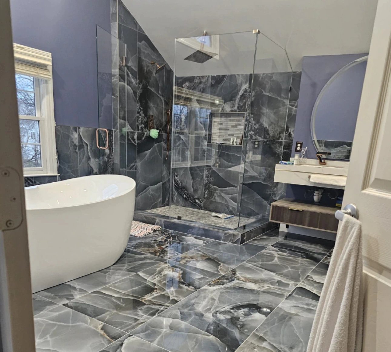 lilac blueish bathroom witha white rounded bath and a shower with glass windows
